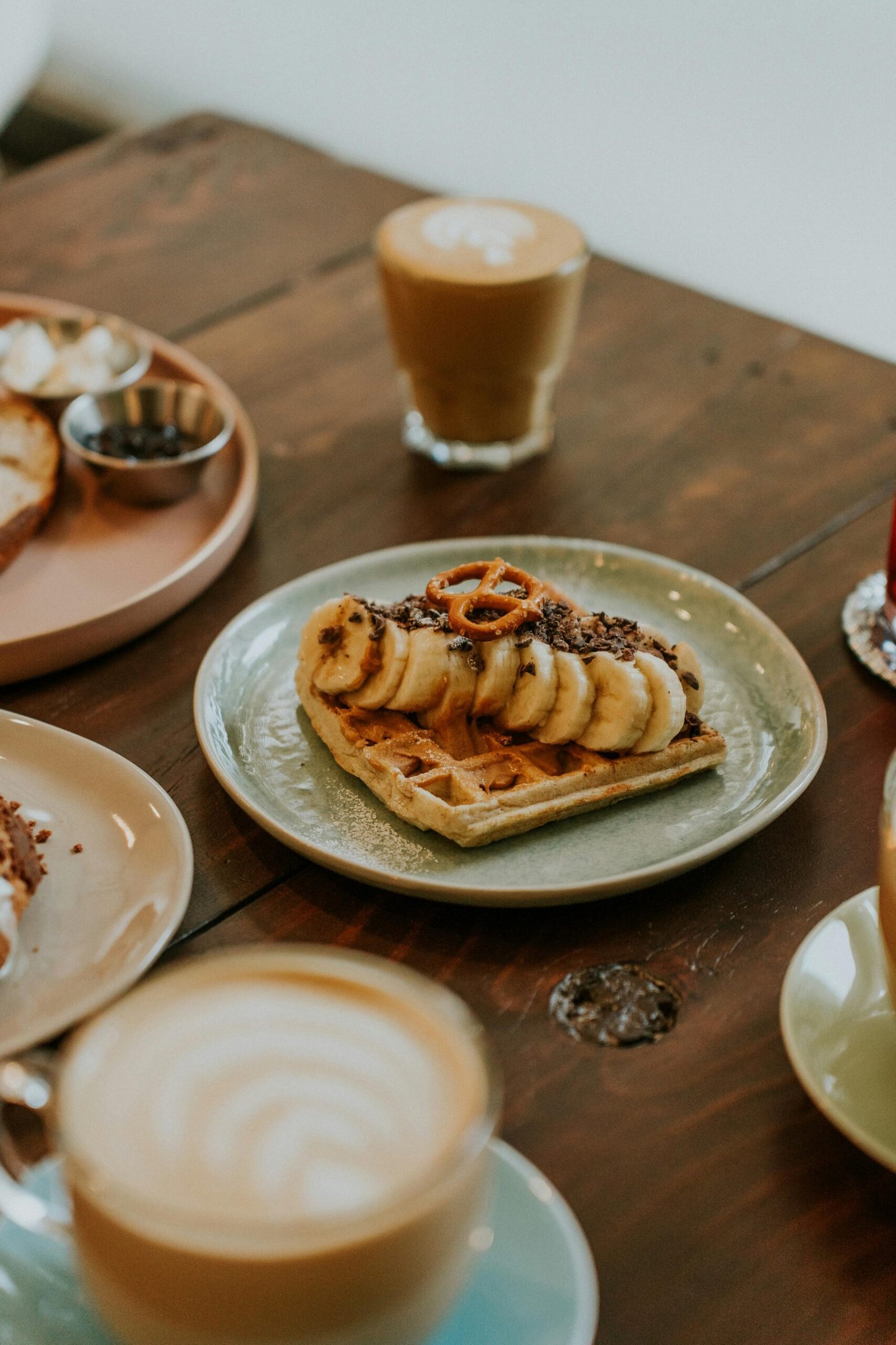 A tasty breakfast spread featuring a waffle topped with banana slices and pretzel, accompanied by hot coffee.